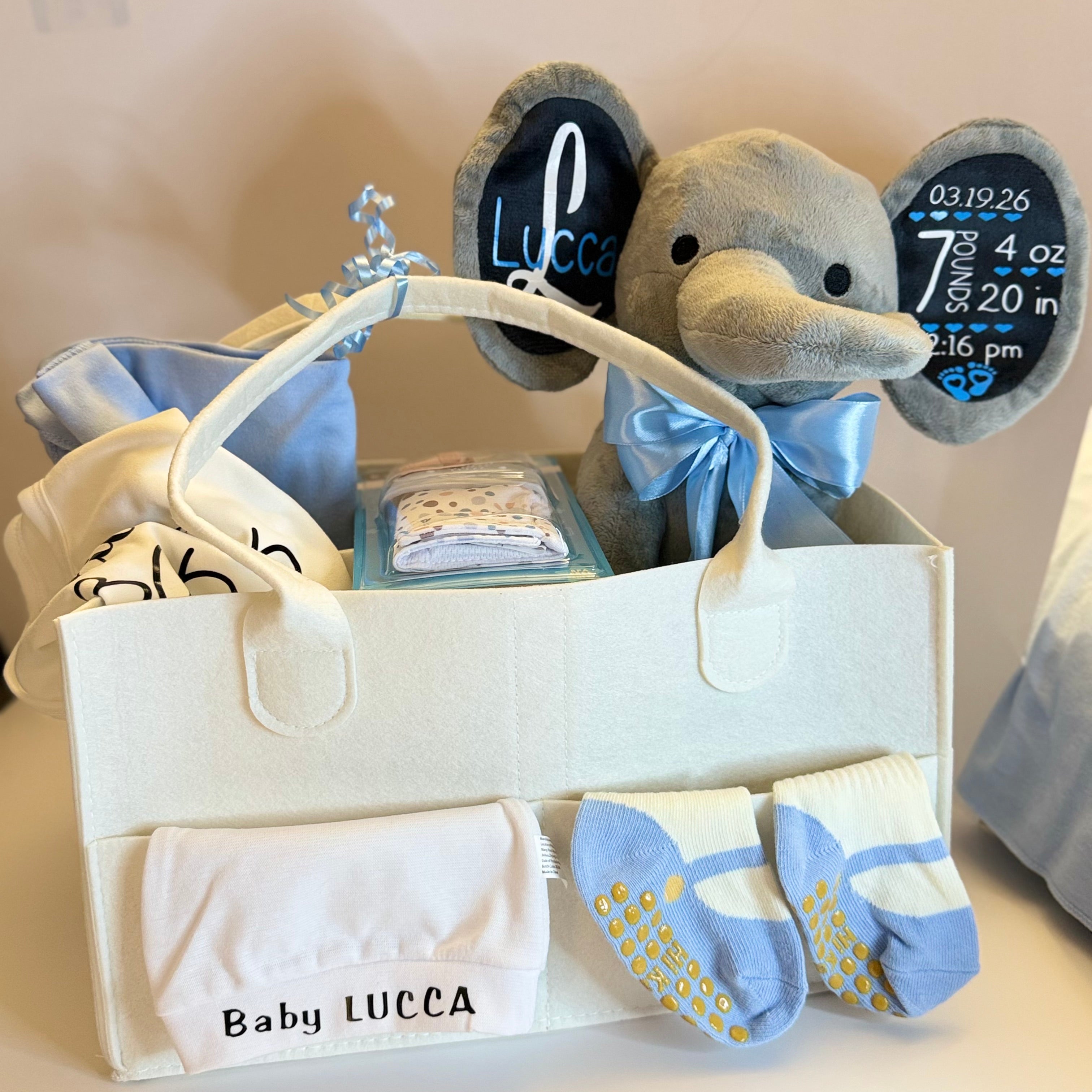 Luxury personalized baby gift basket set in cream and blue tones with a custom stamped elephant and premium newborn essentials.