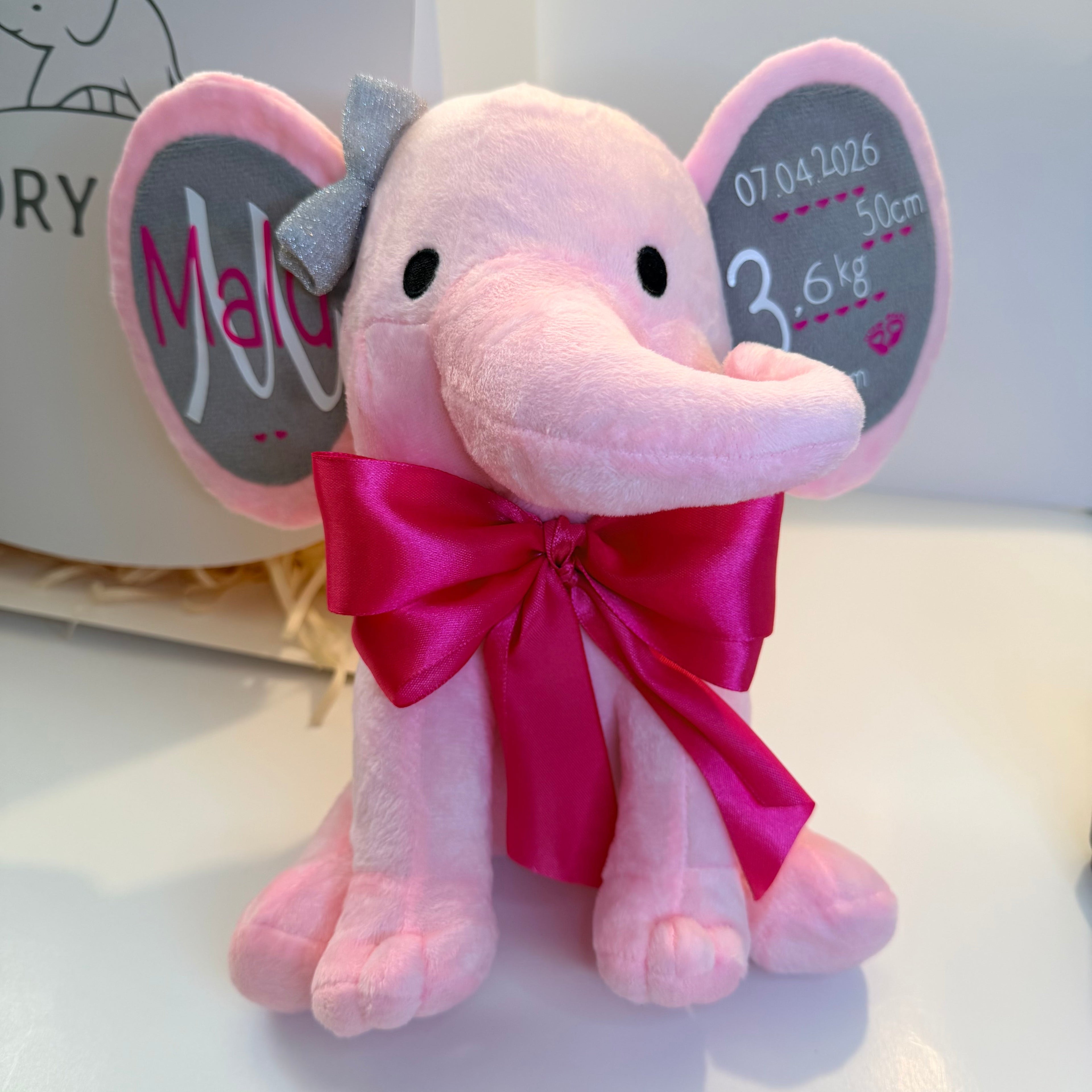 Pink plush elephant toy with a large red bow on a white background