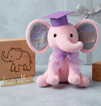 Ivory Heir personalized 9-inch pink graduation elephant plush toy featuring a purple glitter mortarboard cap, matching sheer organza bow, and custom stamped ears with the name Agatha and Class of 2026.