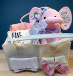 he Grand Welcome Set by Ivory Heir featuring a personalized pink birth stats elephant, custom newborn bodysuit, and luxury baby blanket arranged beautifully in a gift basket.