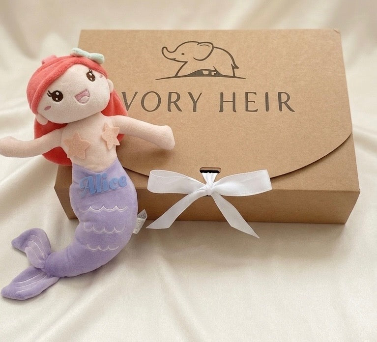 Ivory Heir personalized purple mermaid plush toy sitting next to a signature luxury ivory gift box tied with a white bow.