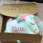 Ivory Heir personalized unicorn plush inside signature gift packaging with a white ribbon.
